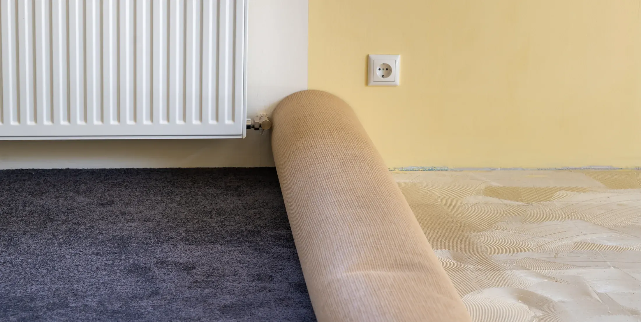 A roll of carpet being unrolled over pad in an empty room
