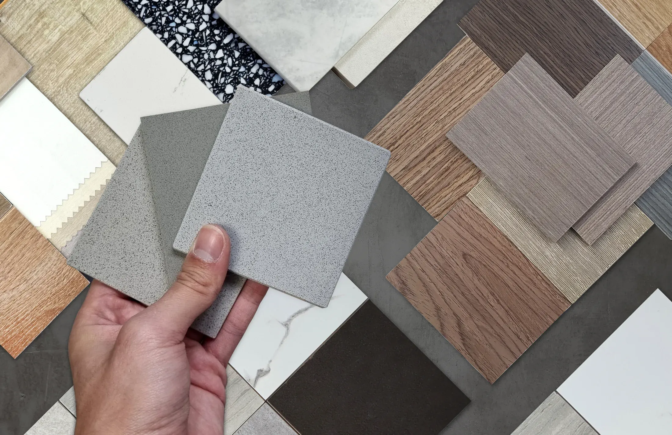Hand holding a stone tile sample above a spread of wood, laminate, and tile flooring samples