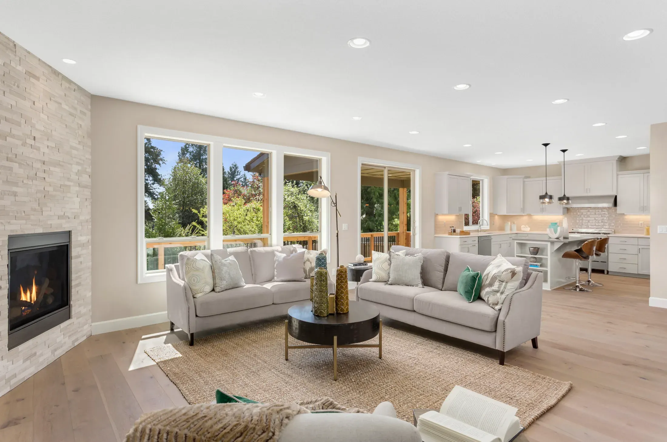 Bright living room with light hardwood flooring, a stone fireplace, and large windows